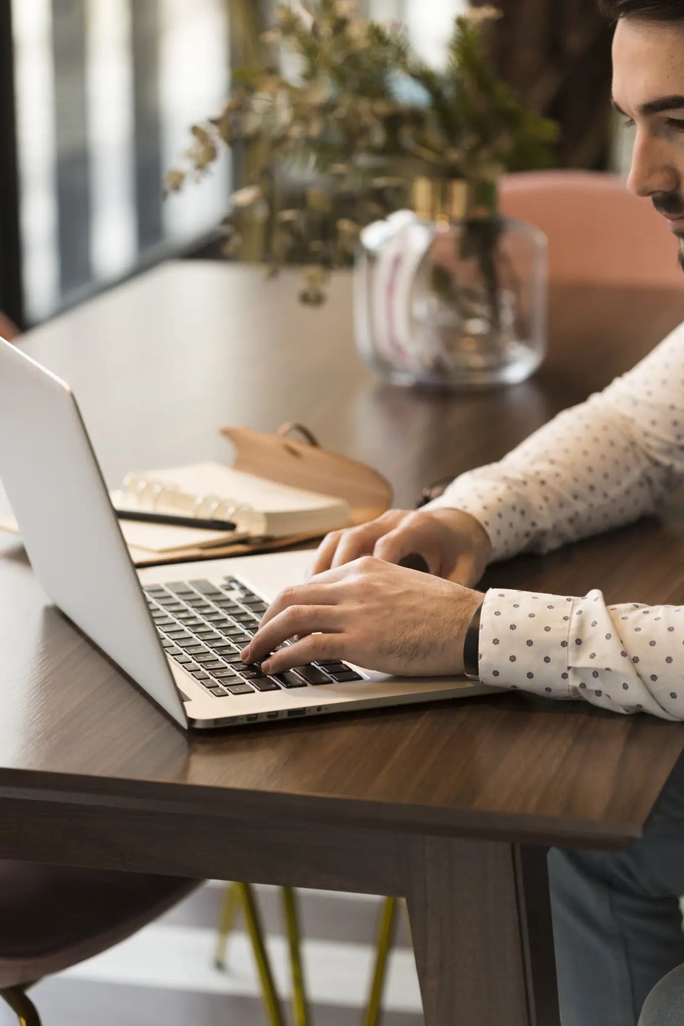 Person using a laptop at a wooden table with a blurred background