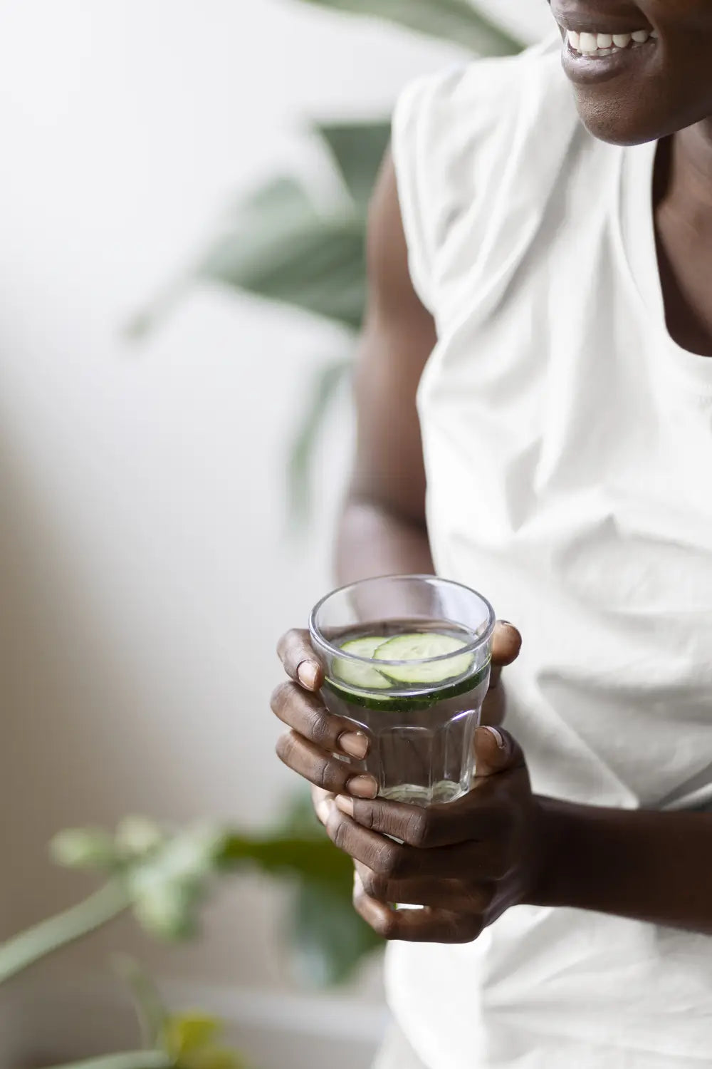 Woman holding a glass of water with floating cucumbers 
